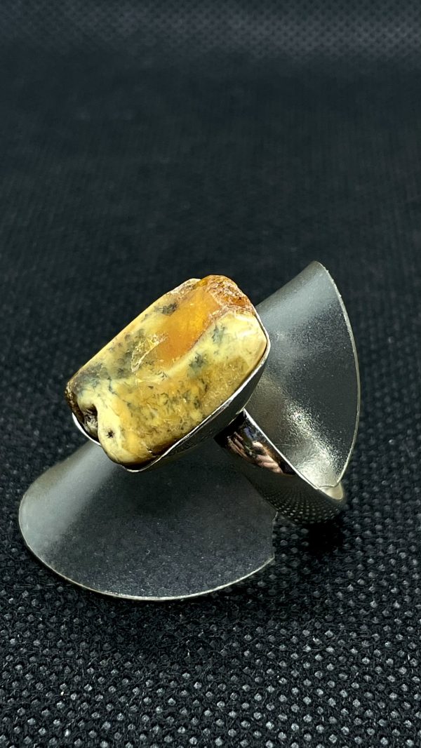 Ring aus 925/- Silber und Bernstein auf einer Ringhalterung und dunklem Untergrund. Das Bild dient der Produktansicht.